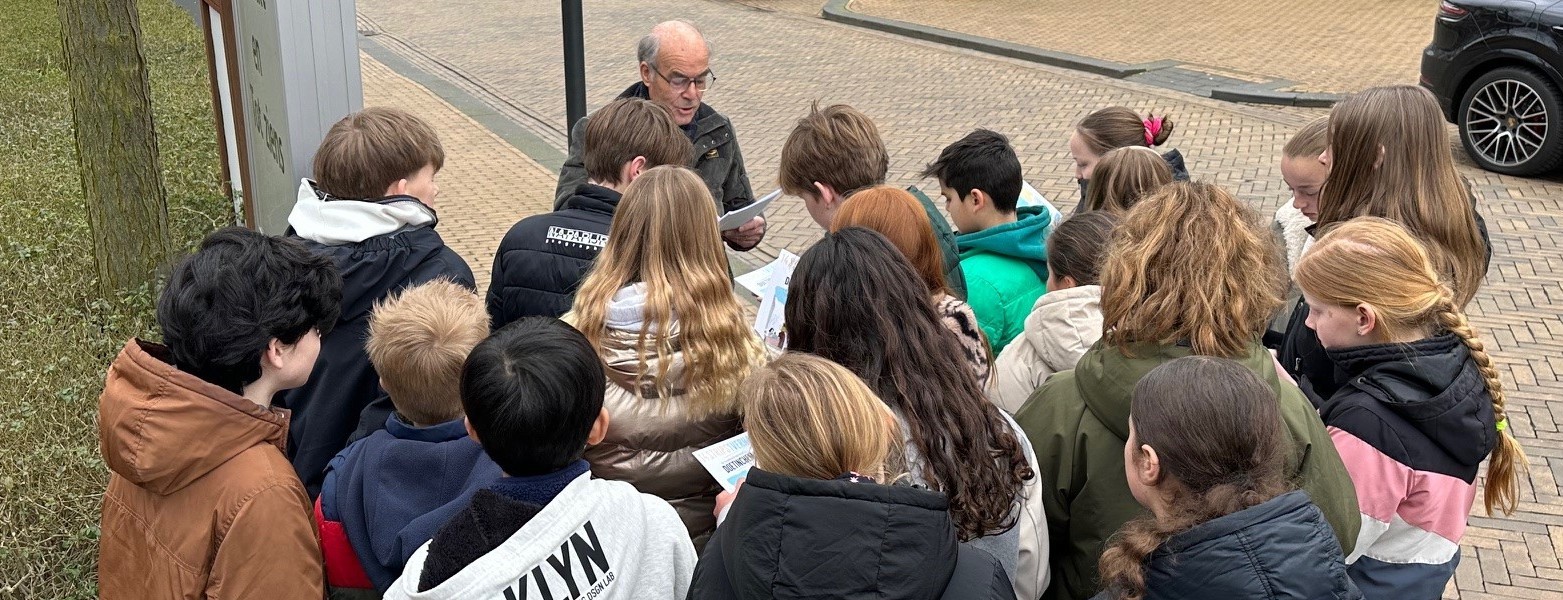 Henk Peters van het Gilde geeft een stadswandeling aan een groep kinderen.