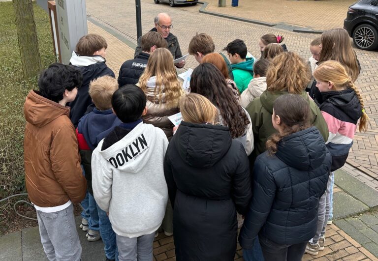 Henk Peters van het Gilde geeft een stadswandeling aan een groep kinderen.